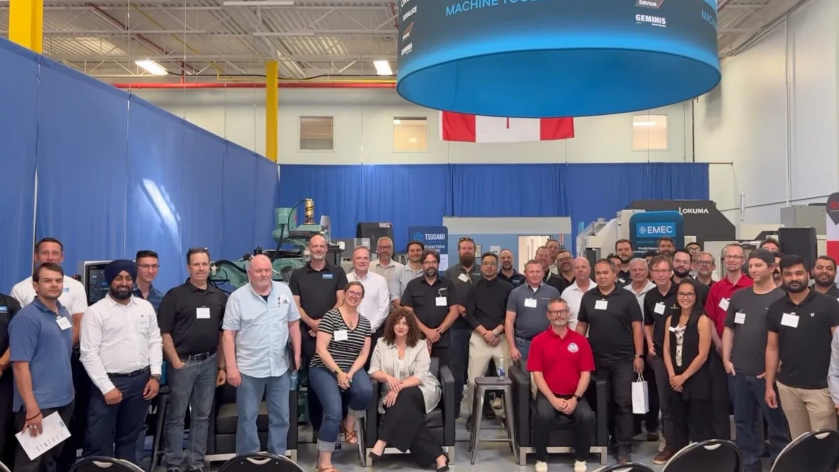 A group of about fifty Ontario Machining Alliance attendees posing together on a machine tool showroom floor.